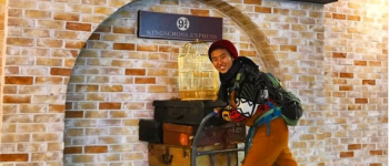 A student pretending to push a Harry Potter style luggage cart into a wall at Kings Cross train station